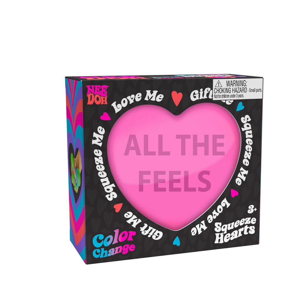 A boxed Nee Doh Color Change Squeeze Heart K3 toy. The packaging is predominantly black with colorful accents, featuring phrases like "ALL THE FEELS," "Squeeze Me," "Love Me," and "Gift Me." The box also includes a choking hazard warning for small parts.